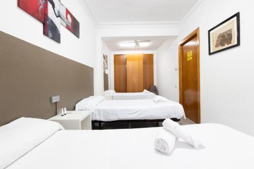 two beds in a room with white sheets at Pensión Galicia in Canovellas