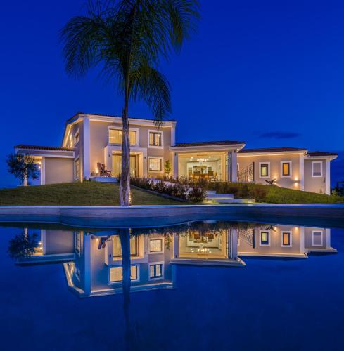 a large house with a palm tree in front of a pool at Villa Shangri-La Zakinthos in Zakynthos Town