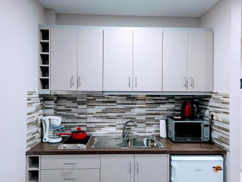 uma cozinha com armários brancos, um lavatório e um micro-ondas em Central Square Apartment 1 em Pirgos