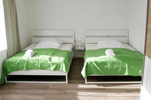 2 Betten mit grüner Bettwäsche in einem weißen Zimmer in der Unterkunft Ferienwohnung Waldvogel in Immenstaad am Bodensee
