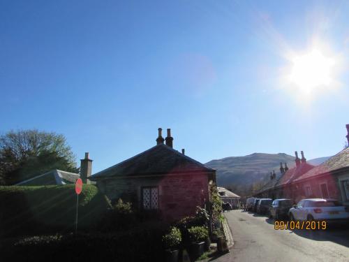 a small brick house on a street with mountains in the background at Levenview Holiday Apartment Loch Lom in Balloch