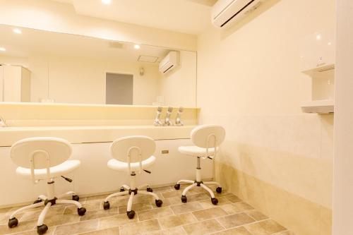 a bathroom with three white chairs and a large mirror at HOTEL THE CUBE Naha Kokusai Street in Naha