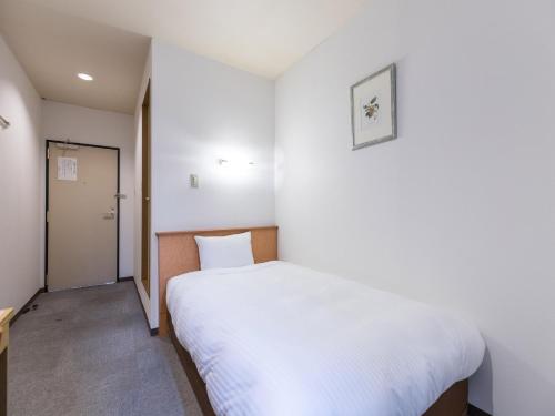 a small bedroom with a white bed and a door at Hotel Isesaki East in Isesaki