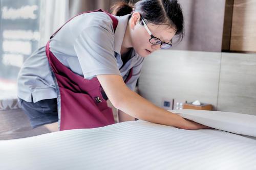 a woman making a bed in a hotel room at Green World Taipei Station in Taipei