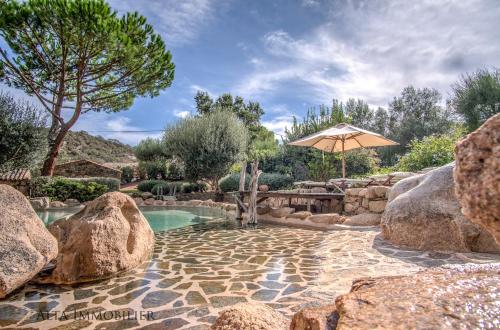 uma piscina com um guarda-sol e rochas em Villa Serenita Pallombaggia em Porto-Vecchio