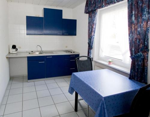 cocina con armarios azules, mesa y ventana en Pension Mosella , Wohnung mit Balkon und Moselblick, en Sankt Aldegund