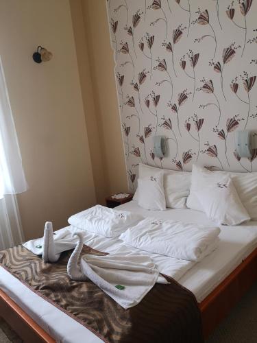a bed with white sheets and a floral wallpaper at Szent István Wellness Panzió in Makó