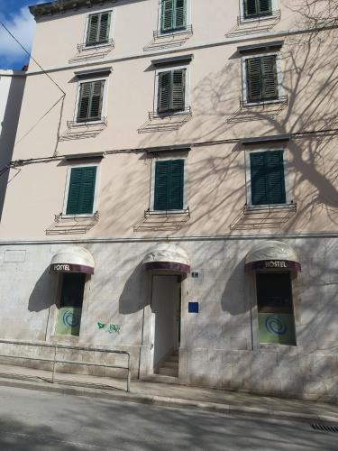 a white building with green shuttered windows on a street at Hurricane Hostel in Split