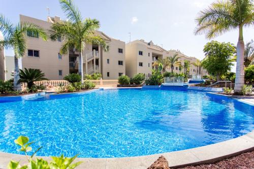 uma grande piscina com palmeiras em frente a um edifício em Laderas del Palmar em Palm-mar