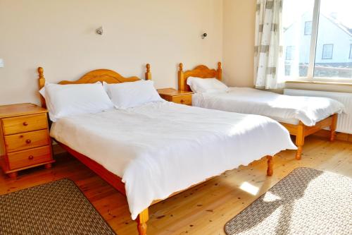 a bedroom with two beds with white sheets and a window at Cois Farraige in Doolin