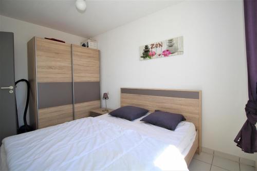ein Schlafzimmer mit einem weißen Bett mit zwei blauen Kissen in der Unterkunft VOILLIERS- T2 avec parking à 700m de la plage in Canet-en-Roussillon