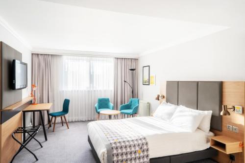 a hotel room with a bed and chairs and a tv at Holiday Inn Hemel Hempstead M1, Jct. 8 by IHG in Hemel Hempstead