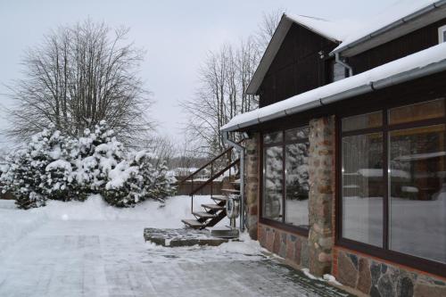 una casa con nieve en el suelo junto a un edificio en Guest House Pilsētnieki, en Slampe