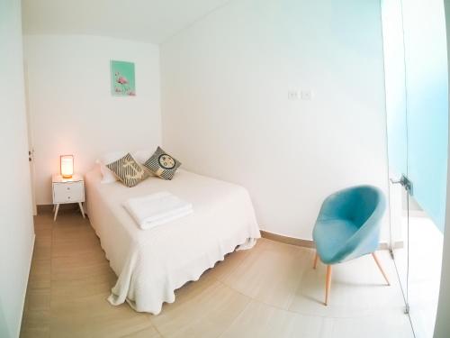 a white bedroom with a bed and a blue chair at Departamento de playa - Condominio OCEAN REEF - SAN BARTOLO in San Bartolo