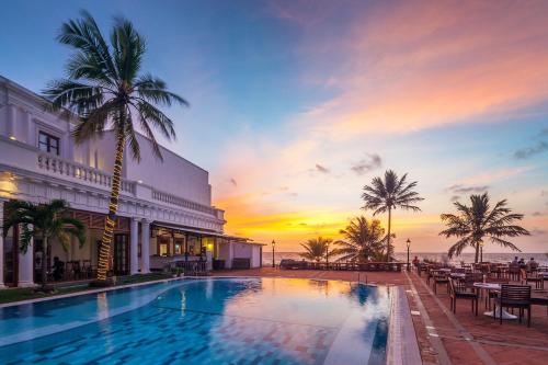 a swimming pool in front of a building with a sunset at Mount Lavinia Hotel in Mount Lavinia