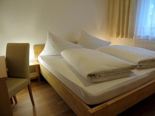 Cette chambre comprend un lit avec des draps blancs et une chaise. dans l'établissement Haus Matt, à Laterns