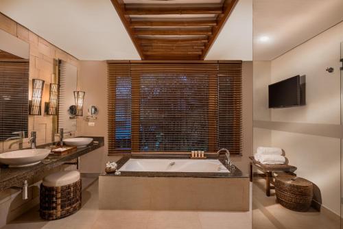 uma casa de banho com uma banheira, 2 lavatórios e uma televisão em Crimson Resort and Spa - Mactan Island, Cebu em Mactan