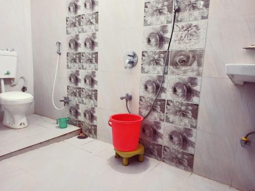 a bathroom with a toilet and a red bucket at Hotel Anand LOK in Rājgīr