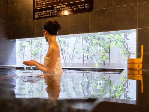 Super Hotel Shinagawa Shinbanba في طوكيو: امرأة جالسة في حوض الاستحمام تنظر من النافذة