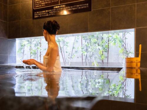 a woman sitting in a bath tub looking out a window at Super Hotel Shinagawa Shinbanba in Tokyo