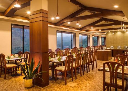 een eetkamer met tafels, stoelen en ramen bij Abad Copper Castle Resort in Munnar