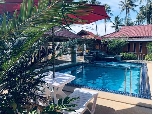 a swimming pool with two chairs and a red umbrella at Chuu Pun Village Resort in Pantai Cenang