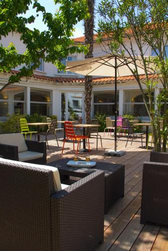 a patio with chairs and tables and an umbrella at Hôtel Le Vert Bois in Dolus d'Oléron