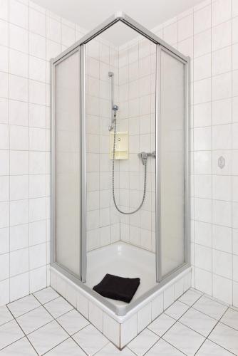 a shower in a white tiled bathroom with a black towel at Ferienwohnung Backbord in Carolinensiel