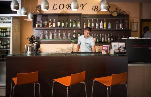 a man standing behind a bar with orange chairs at Hotel Plamena Palace in Primorsko