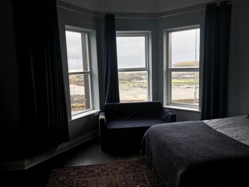 a bedroom with a bed and a chair and windows at Rolling Wave Guesthouse in Bundoran