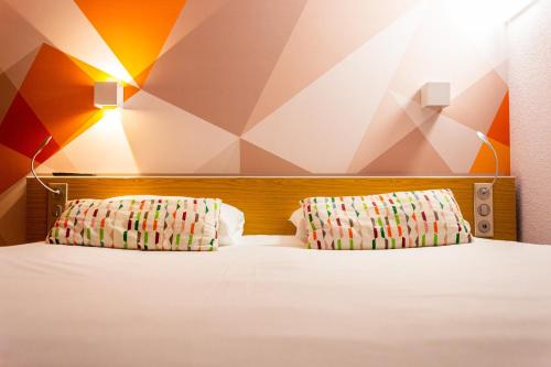 a bedroom with a white bed with two pillows at initial by balladins La Roche-sur-Yon in La Roche-sur-Yon