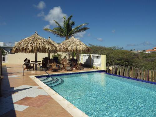 鷹海灘的住宿－阿魯巴昆庫公寓式酒店，一个带两把稻草遮阳伞的游泳池和一个度假村