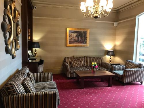 a living room with couches and a table and a chandelier at Belmont Hotel Leicester in Leicester