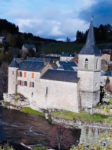 an old building with a church next to a river at Camping Chez Prosper in Fournels