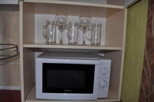 a shelf with glasses and wine glasses on top of a microwave at Cozy apartments near the McDonalds in Kremenchuk