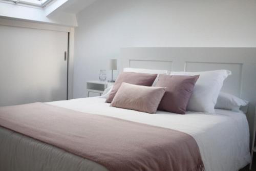 um quarto com uma grande cama branca com almofadas cor-de-rosa em Apartamento Noia Centro Izqda em Noya