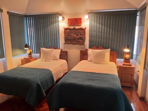 a bedroom with two beds and two lamps and windows at Mirador de Bellavista Riobamba in Riobamba