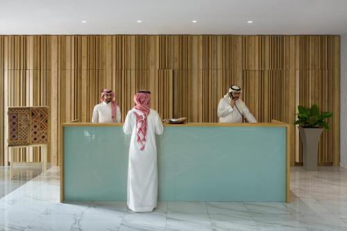 Una donna in piedi davanti a un bancone con due uomini di Adagio Jeddah City Center a Gedda