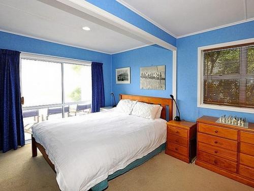 - une chambre bleue avec un grand lit et une fenêtre dans l'établissement Carmens Beachside Bach - Waihi Beach Bach, à Waihi Beach