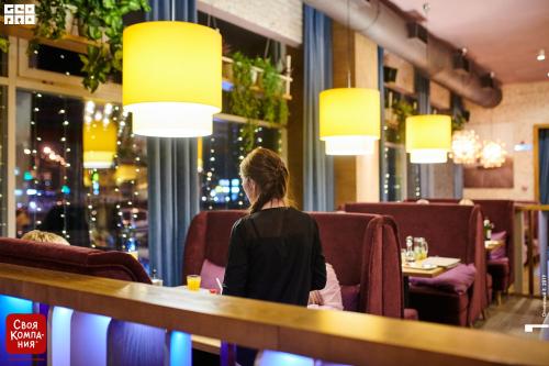 a woman sitting at a bar in a restaurant at Business Hotel in Magnitogorsk