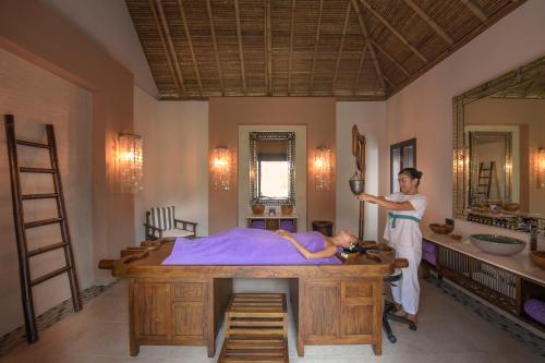 a woman standing next to a bed with a woman laying on it at Emerald Maldives Resort & Spa-Deluxe All Inclusive in Raa Atoll