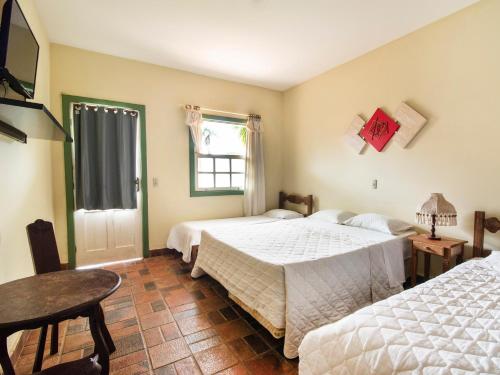 a bedroom with two beds and a table and a window at Pousada Serra Do Ouro in Tiradentes