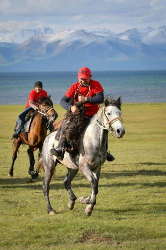 two people riding horses in a field near the ocean at Yurt Camp Ali-Nur, Lake Song-Kul , Kyrgyzstan, Юрточный лагерь Али Нур, на берегу озера Сон Кол in Naryn