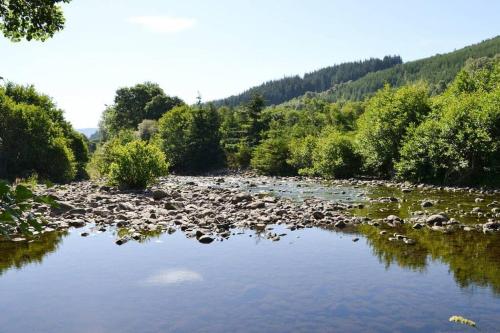 a river with a bunch of rocks and trees at Herons Rest in Drumnadrochit