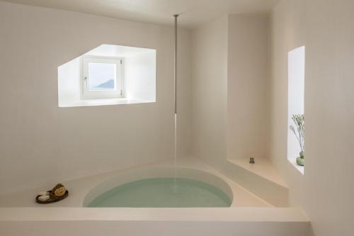 a white bathroom with a tub with a window at The Saint Hotel in Oia