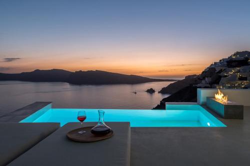 a glass of wine sitting on a table next to a pool at The Saint Hotel in Oia