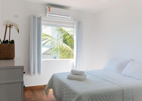 a white bedroom with a bed and a window at Casa Arraial do Cabo Beachfront in Arraial do Cabo