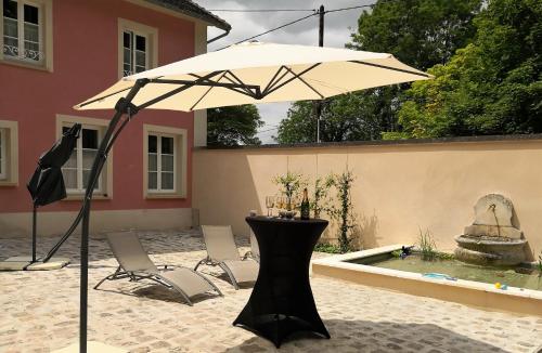 een tafel en stoelen onder een parasol naast een zwembad bij Les 7 Sources in LʼIsle-Adam