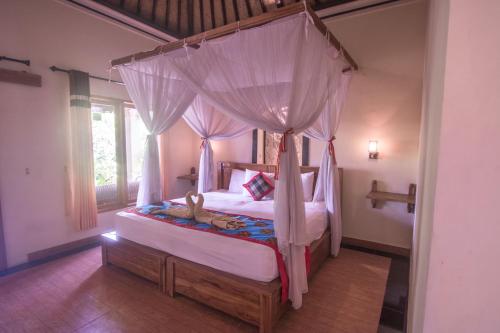 a bedroom with a canopy bed and a window at Trijaya Guest House Pemuteran in Pemuteran