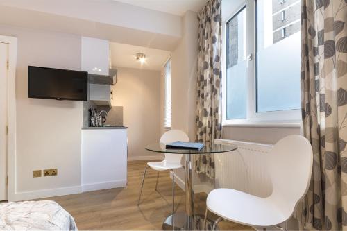 ein kleines Apartment mit einem Glastisch und weißen Stühlen. in der Unterkunft Chelsea Cloisters in London